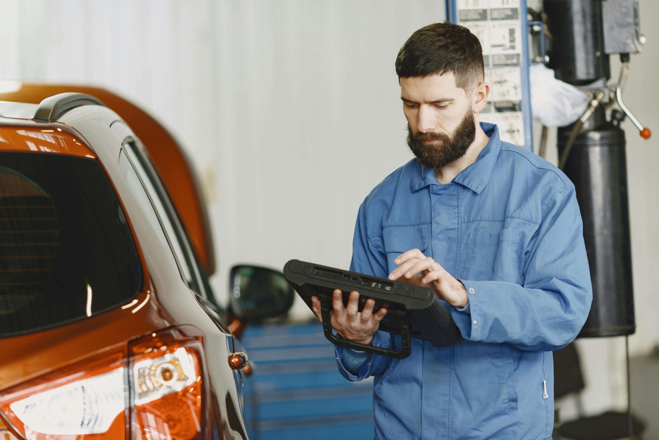 Mechanic in blue uniform using a diagnostic tool on an orange car in a repair shop