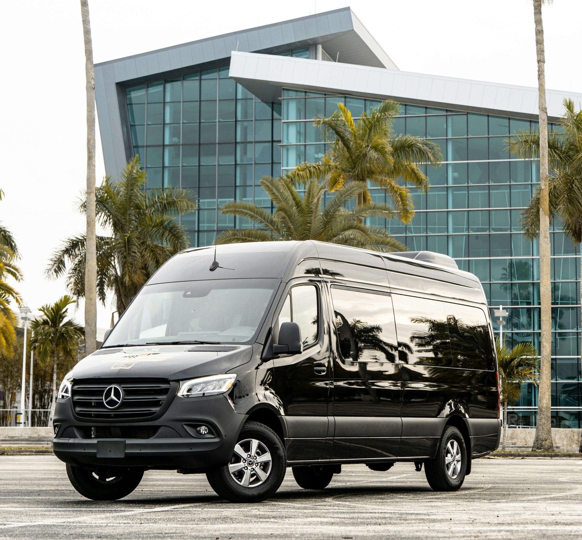 Black Mercedes-Benz Sprinter van parked in front of a modern building with palm trees.