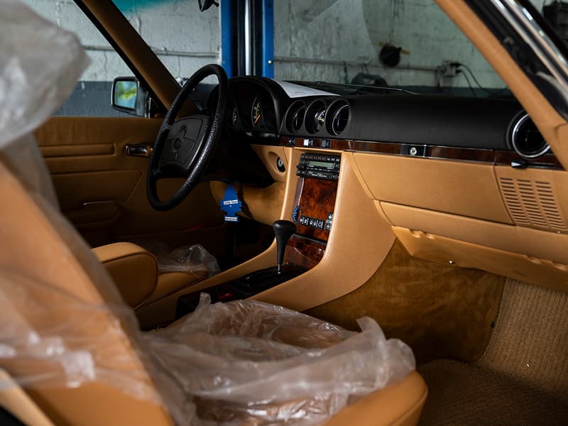 Tan leather interior of a classic Mercedes-Benz SL under protective plastic in the workshop.