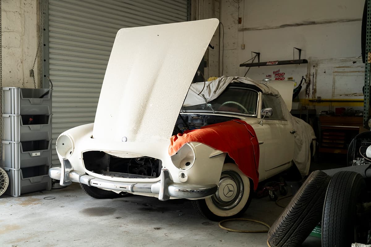 White classic Mercedes-Benz roadster with its hood open and a protective cover over the fender at Miami Benz.