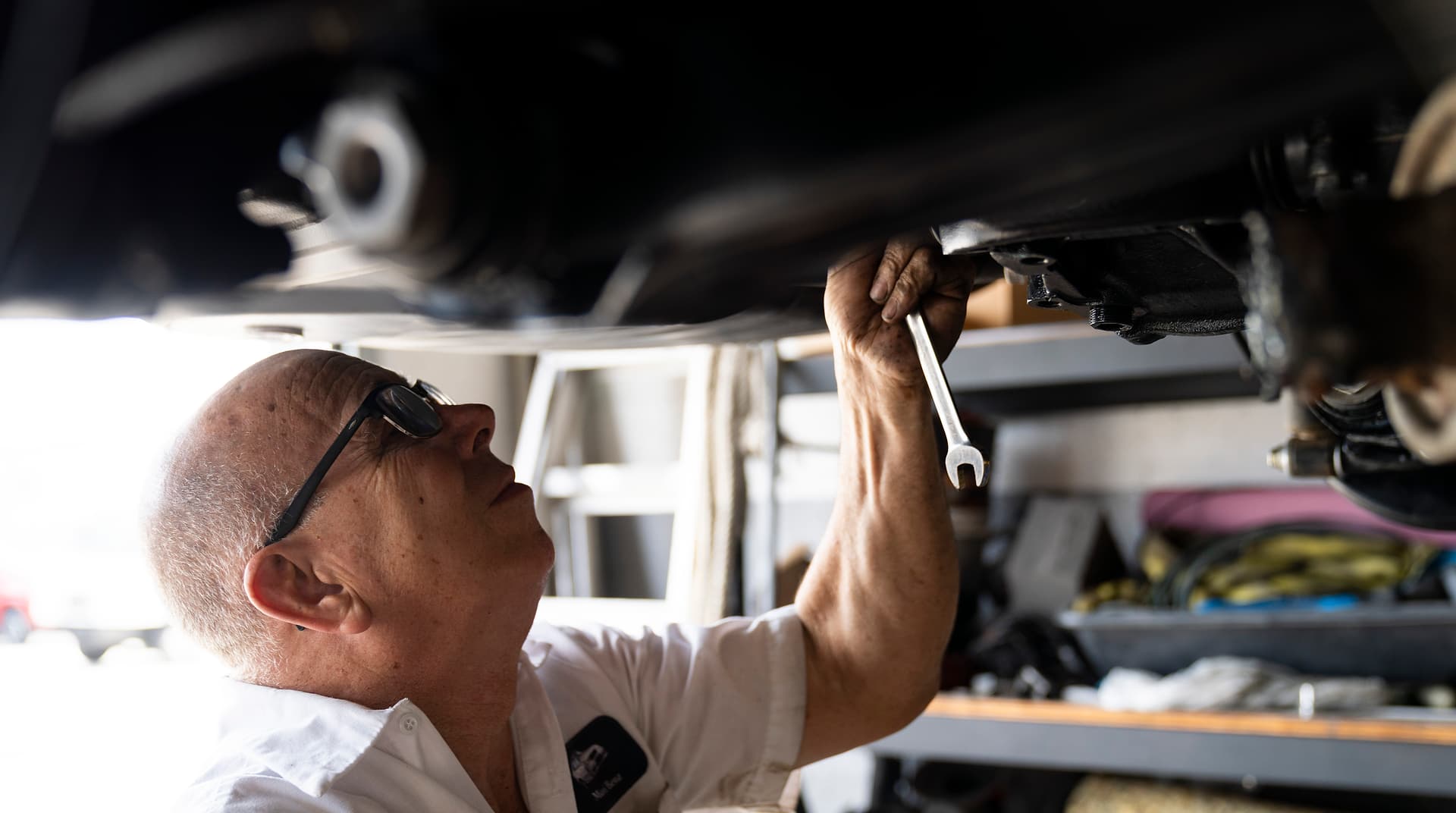 Miami Benz technician with a wrench, inspecting the underside of a car on a lift in the South Miami workshop.