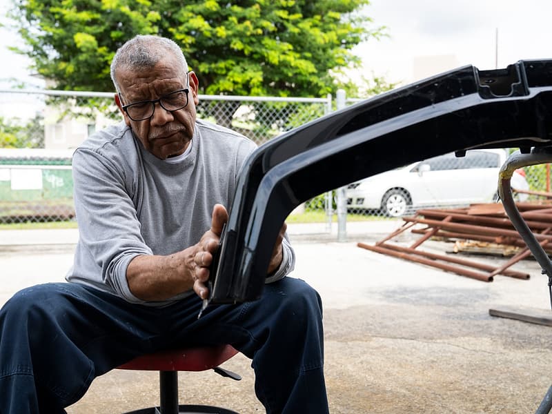 Miami Benz technician working by hand on a black bumper outside the South Miami workshop.